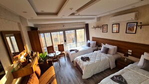 Quarto de hotel com duas camas, área de refeições e janelas amplas.