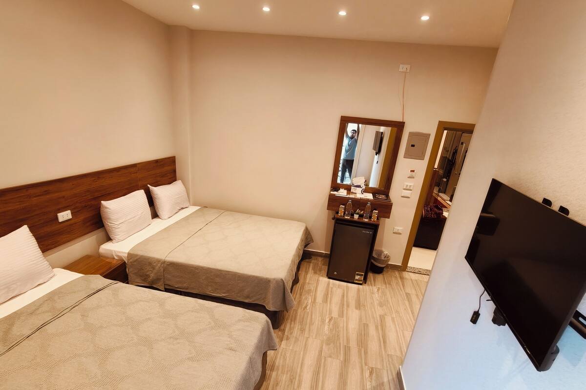 A hotel room with two beds, a small refrigerator, a mirror, and a TV.