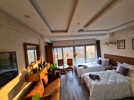Habitación de hotel con sofá, dos camas, televisión, escritorio y vistas al balcón.