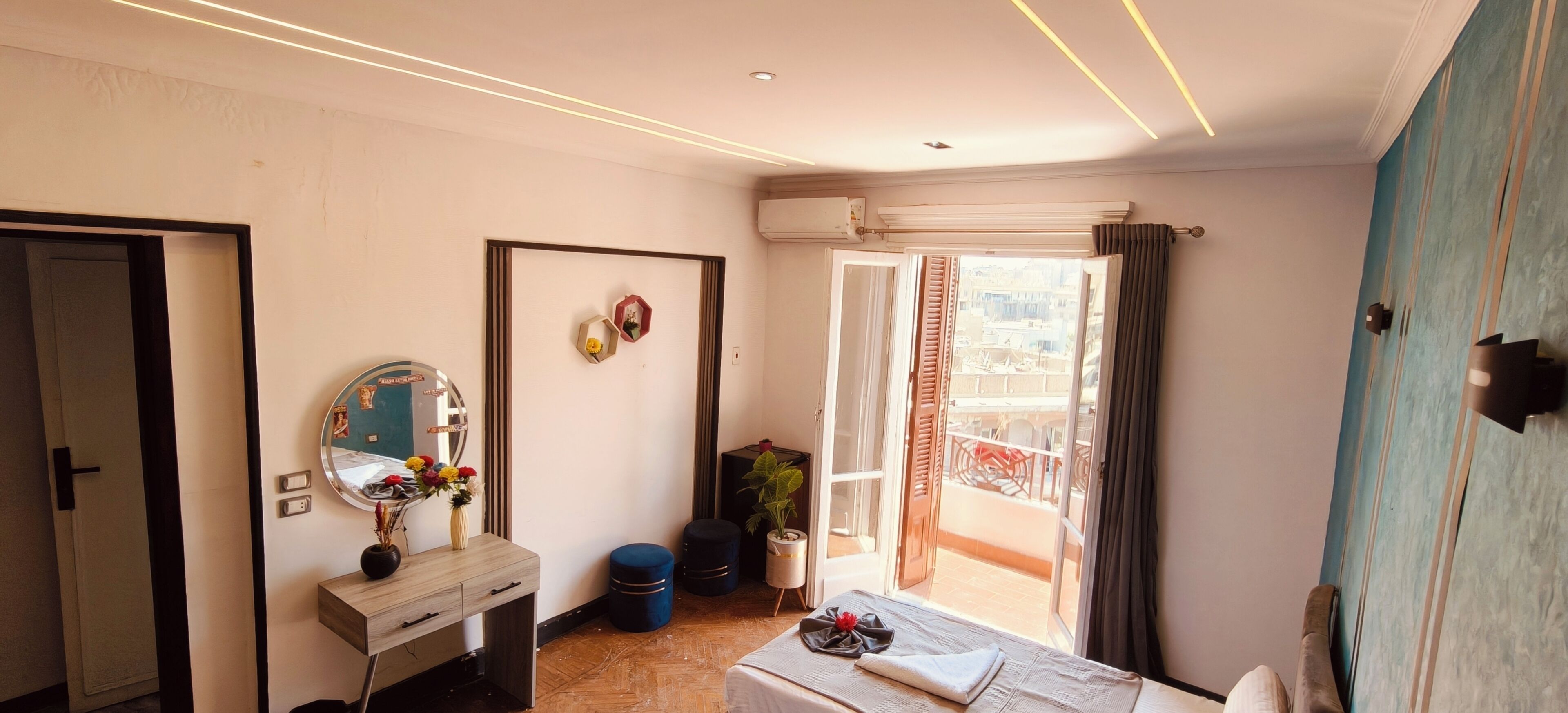 A hotel room with a bed, a dresser, a mirror, a potted plant, and a view of the outside.