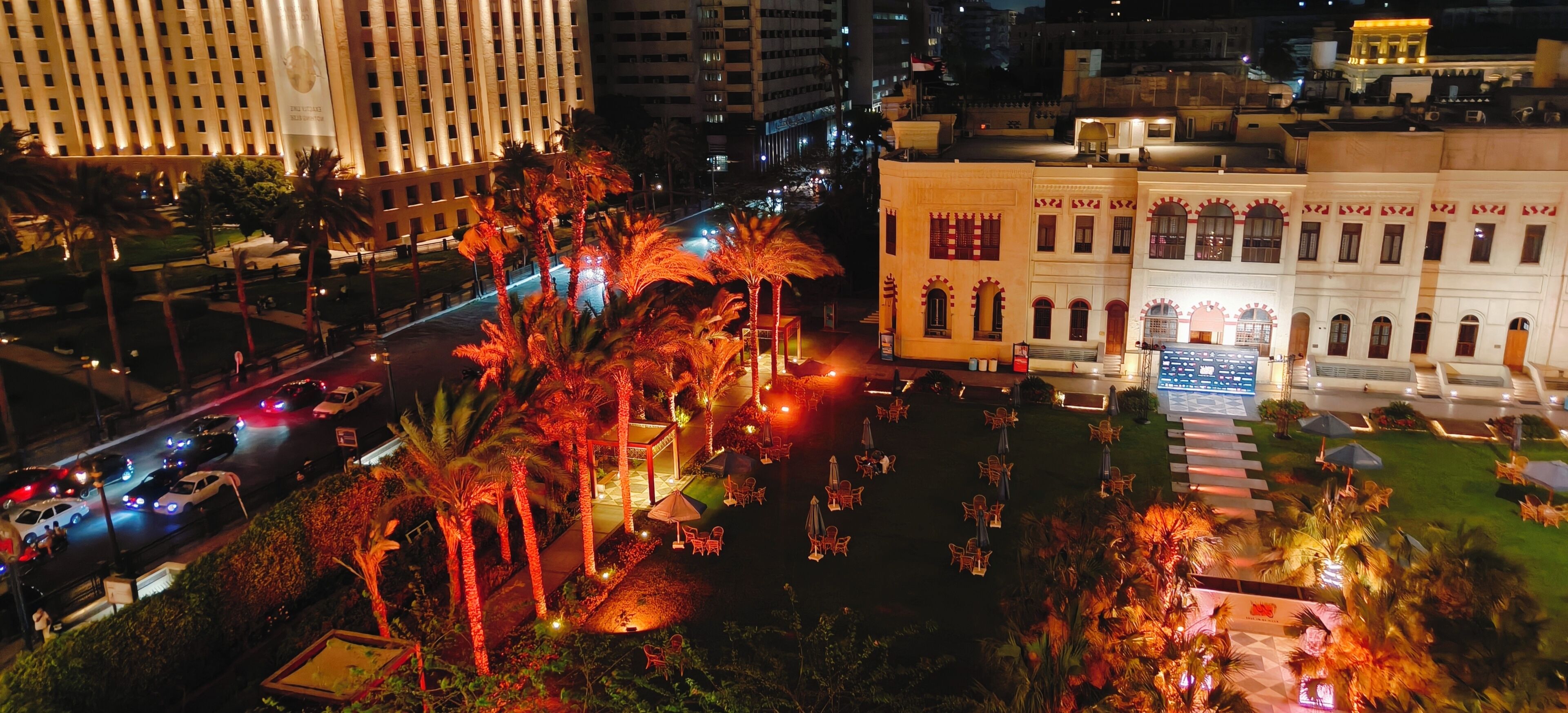 Un hôtel doté d’une cour intérieure, de palmiers et offrant une vue sur la rue la nuit.