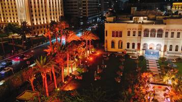 Un hôtel doté d’une cour intérieure, de palmiers et offrant une vue sur la rue la nuit.