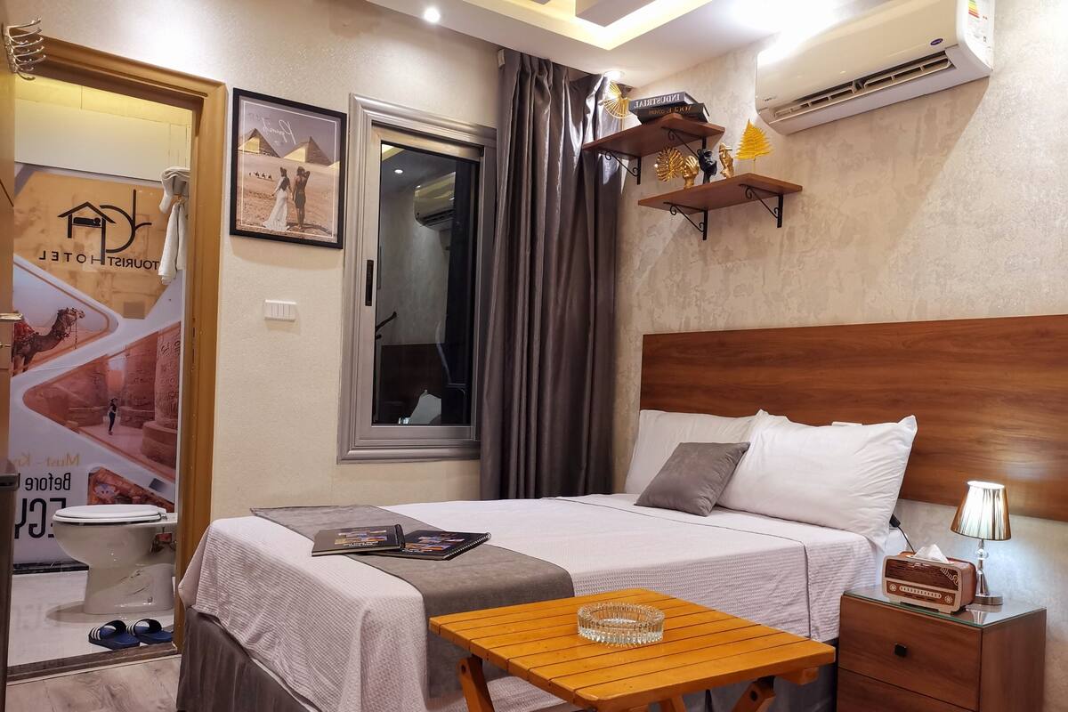 A hotel room with a bed, bedside table, nightstand, and a poster on the wall.