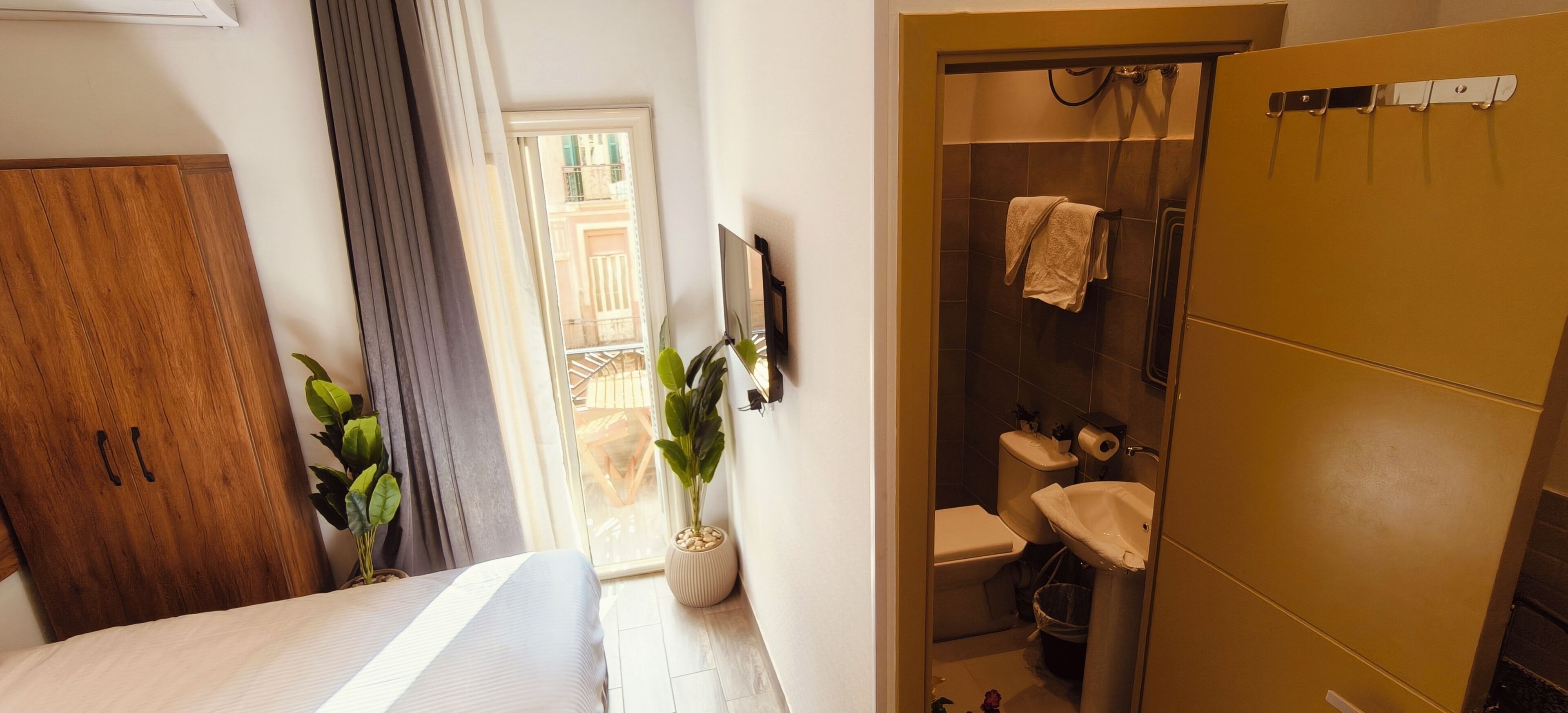 Un dormitorio con cama, armario de madera, planta en maceta y baño completo con ducha, inodoro y lavabo.
