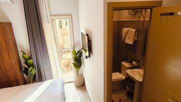Un dormitorio con cama, armario de madera, planta en maceta y baño completo con ducha, inodoro y lavabo.
