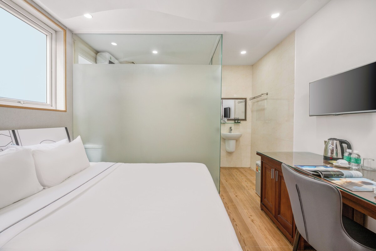 A hotel room with a bed, a desk, a mirror, a TV, and a shower area.