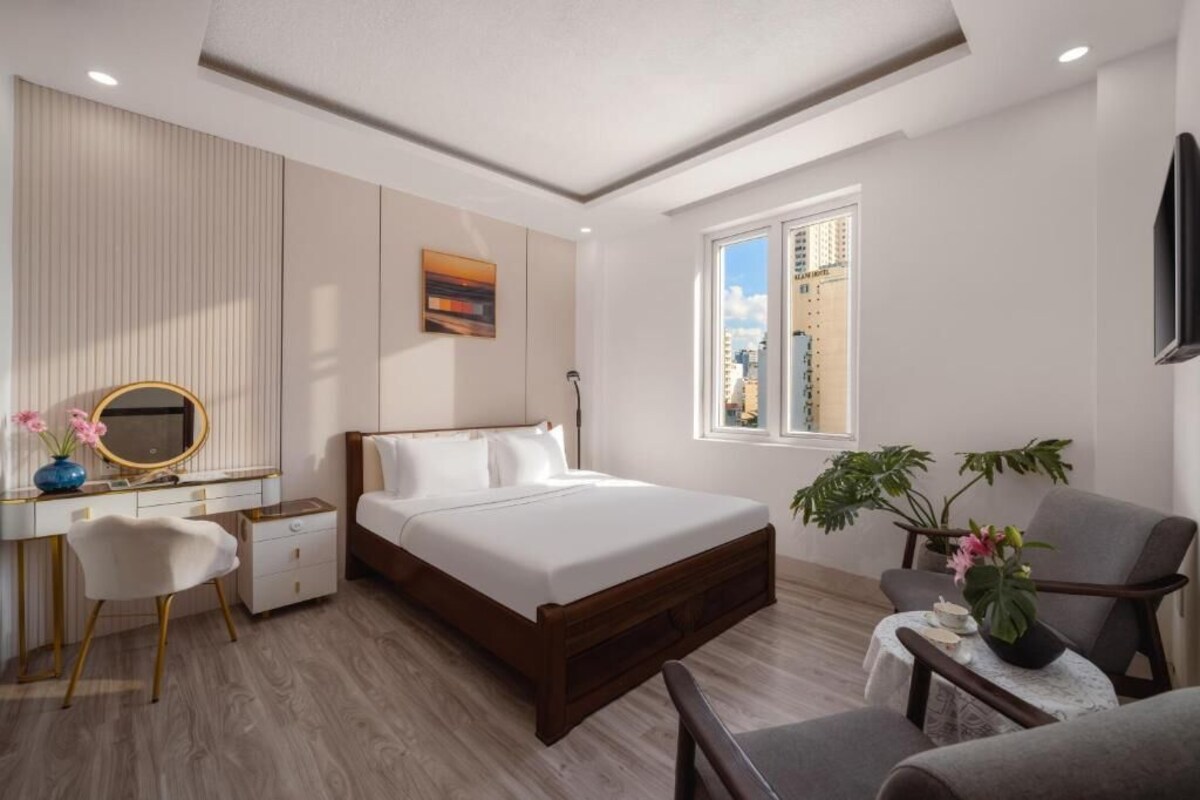 A modern hotel room with a bed, desk, chair, and a view of the cityscape.