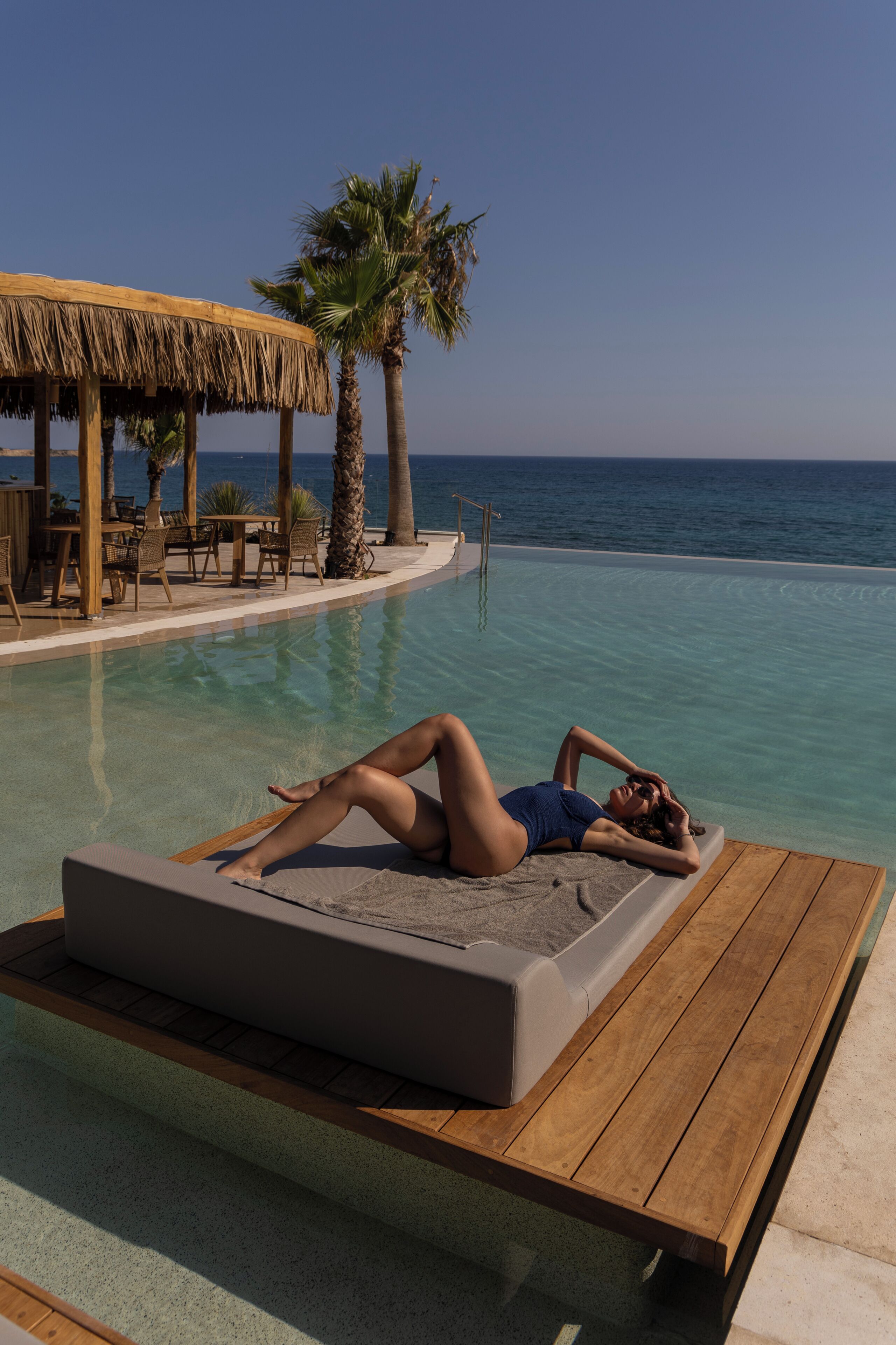 A person lying on a lounge chair by a poolside with a view of the ocean.