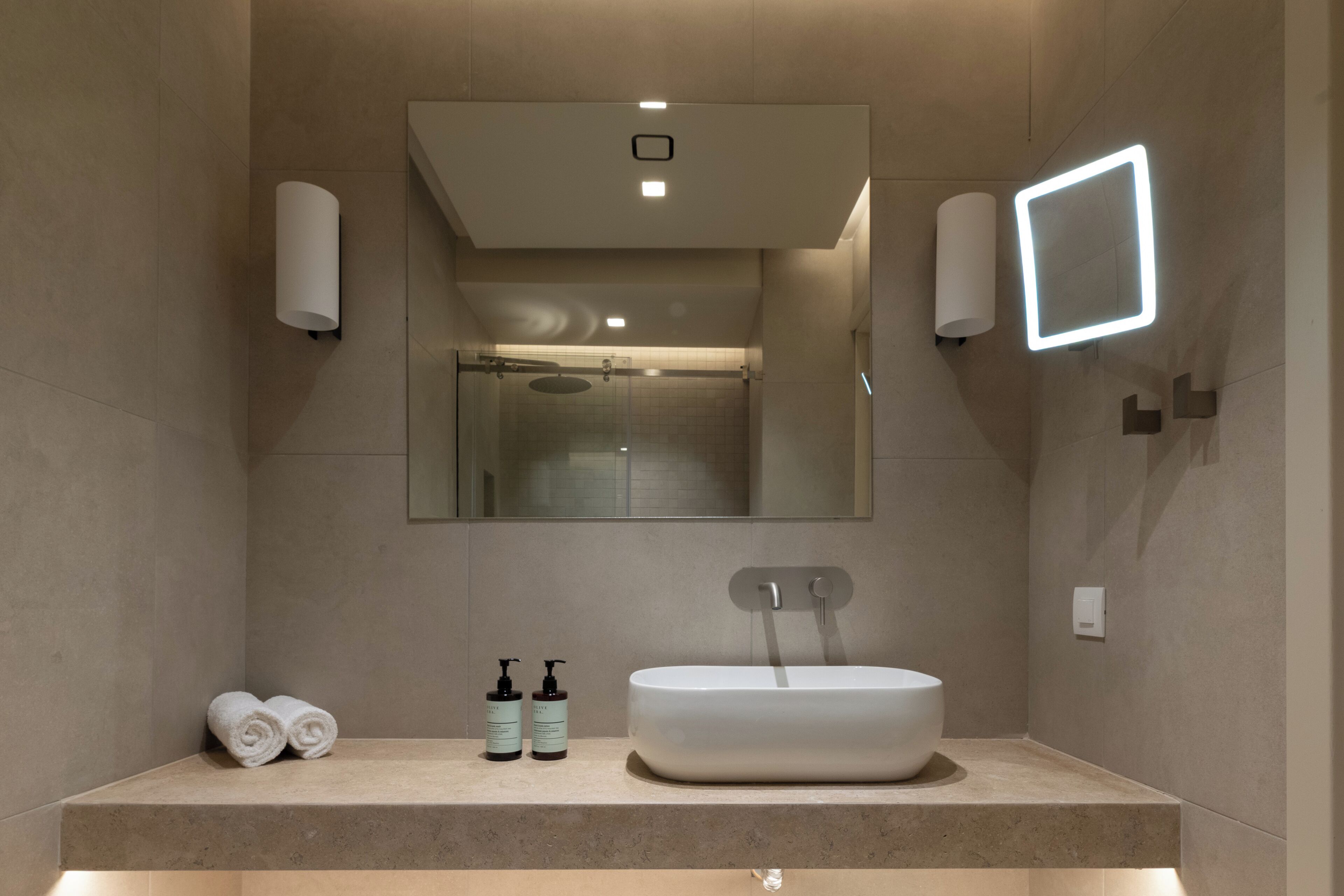 A modern bathroom with a large mirror, a built-in sink, and two towel rolls.