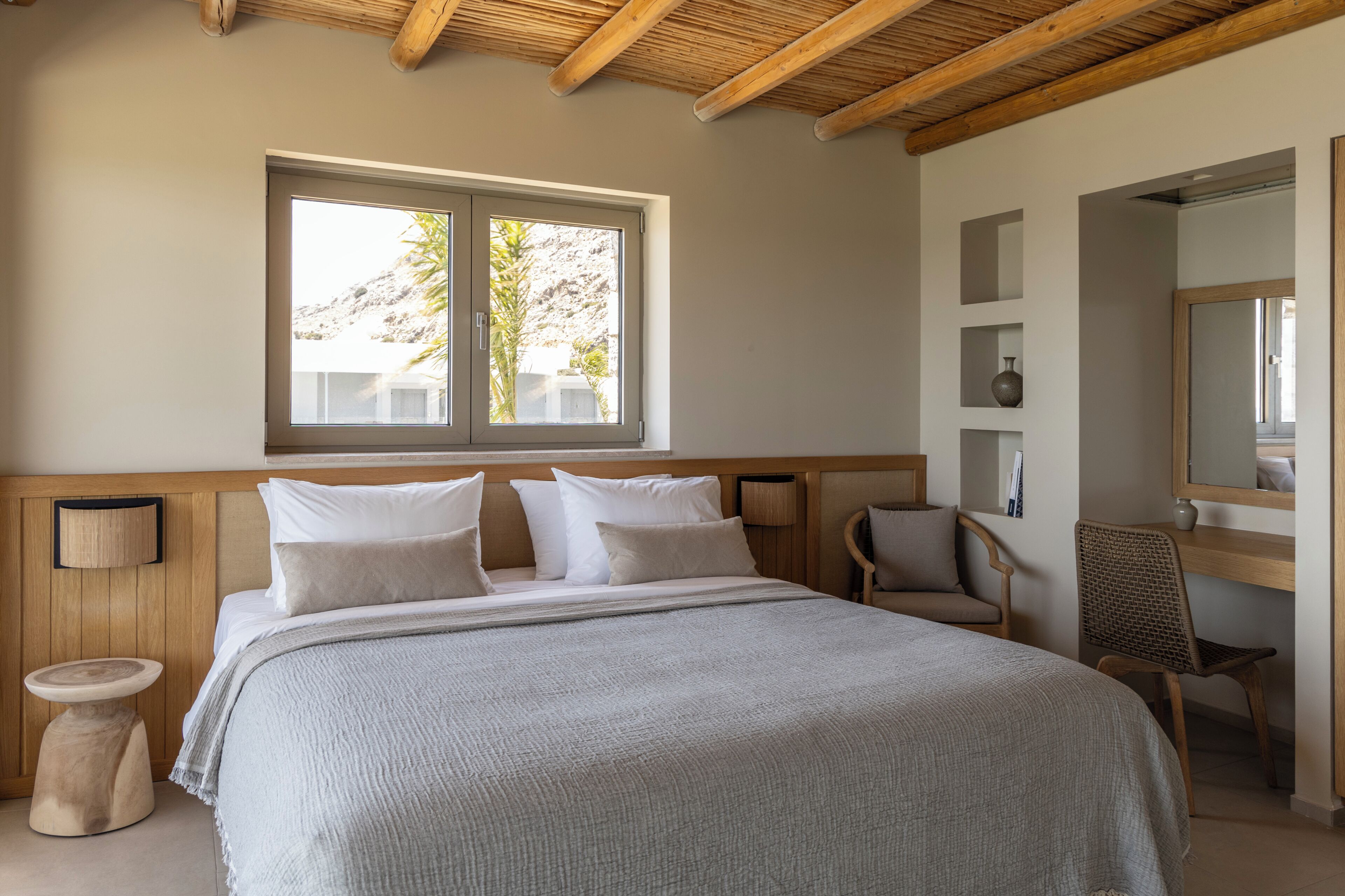 Une chambre à coucher avec un grand lit, une fenêtre donnant sur un beau paysage, un fauteuil et une table de chevet.