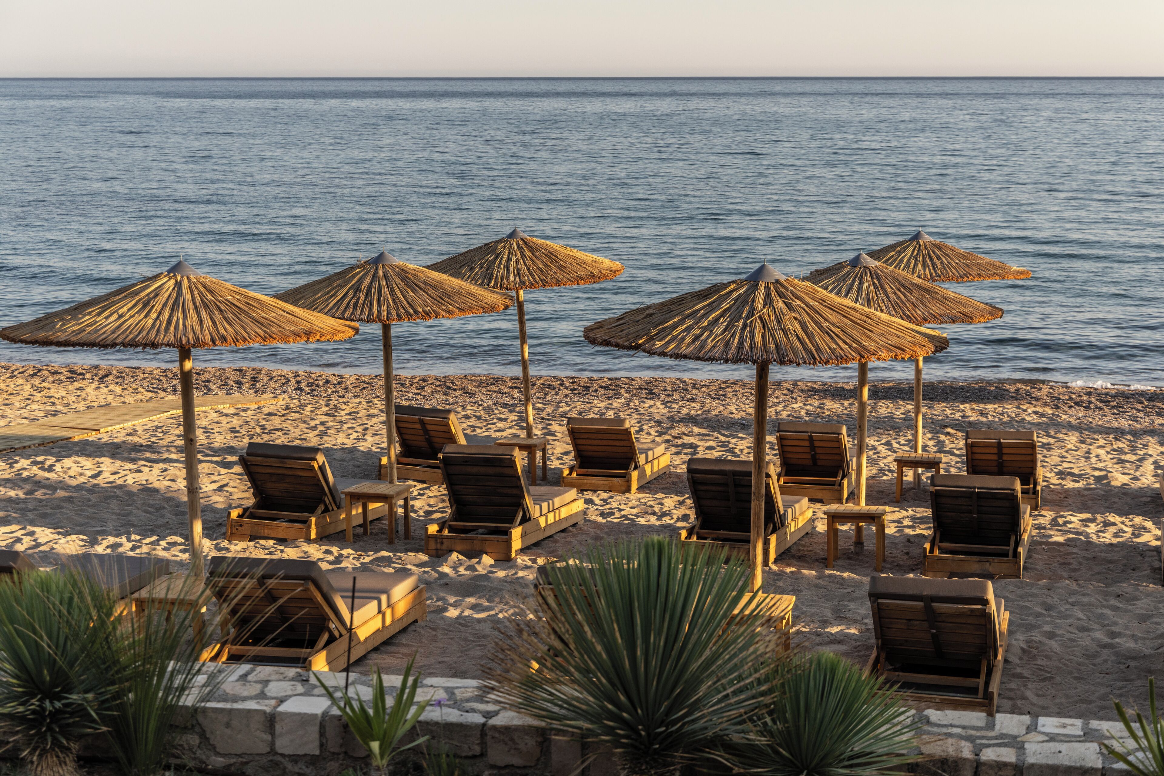 Una playa con sillones de madera y sombrillas de paja.