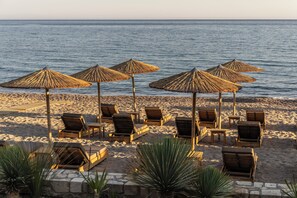 Una playa con sillones de madera y sombrillas de paja.