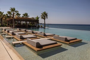 Zona junto a la piscina con sillones de descanso y una barra con techo de paja.