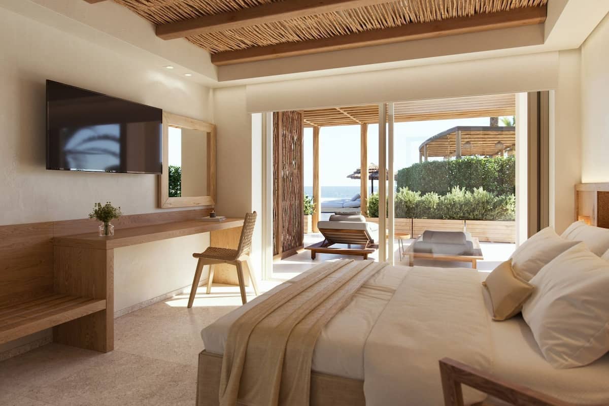A bedroom with a bed, a desk, a chair, a TV, and a view of the outdoors.