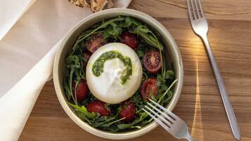Una mesa de madera con un tazón de ensalada, una copa de vino blanco, un tenedor y una servilleta.