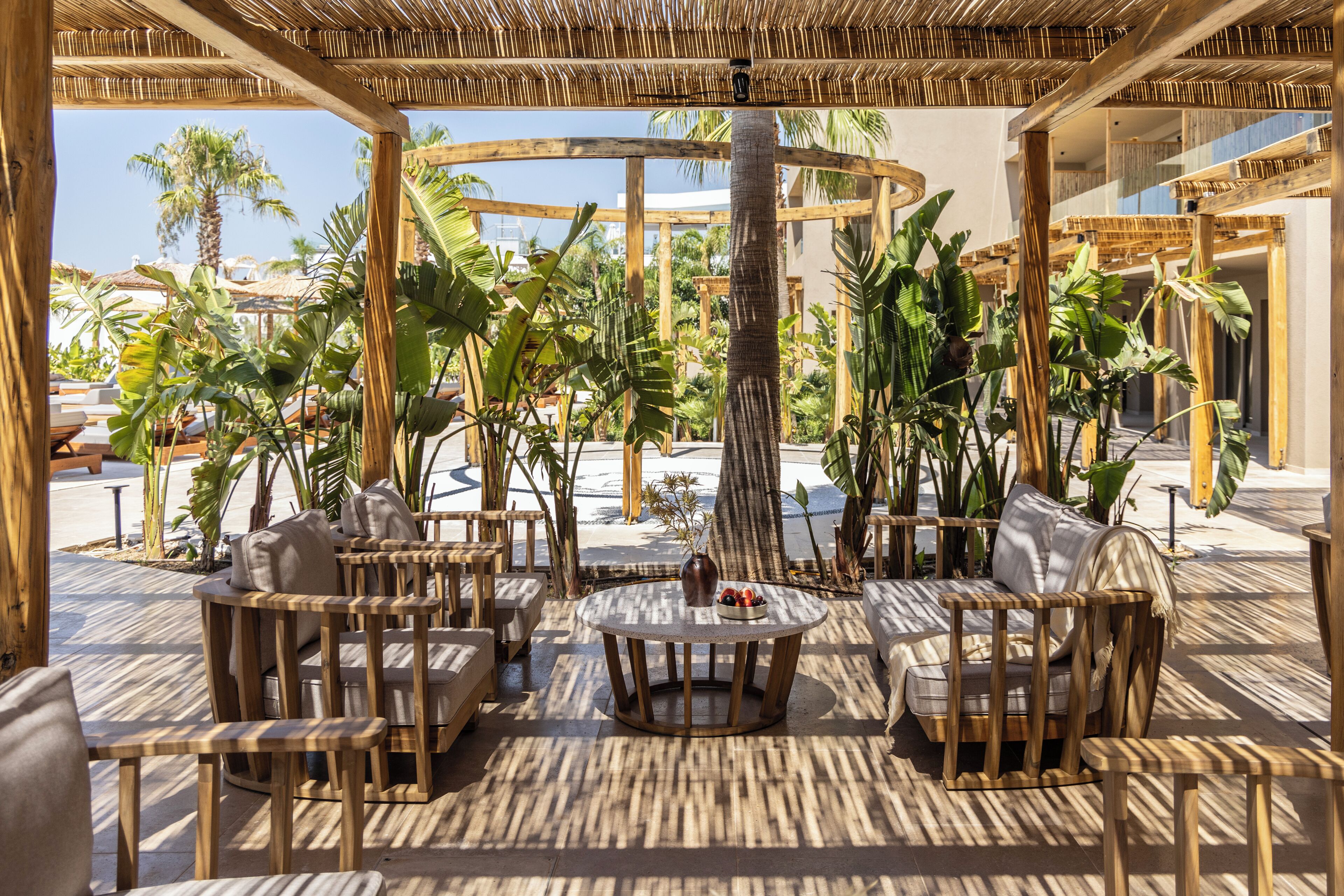 An outdoor seating area with wooden furniture and tropical plants.