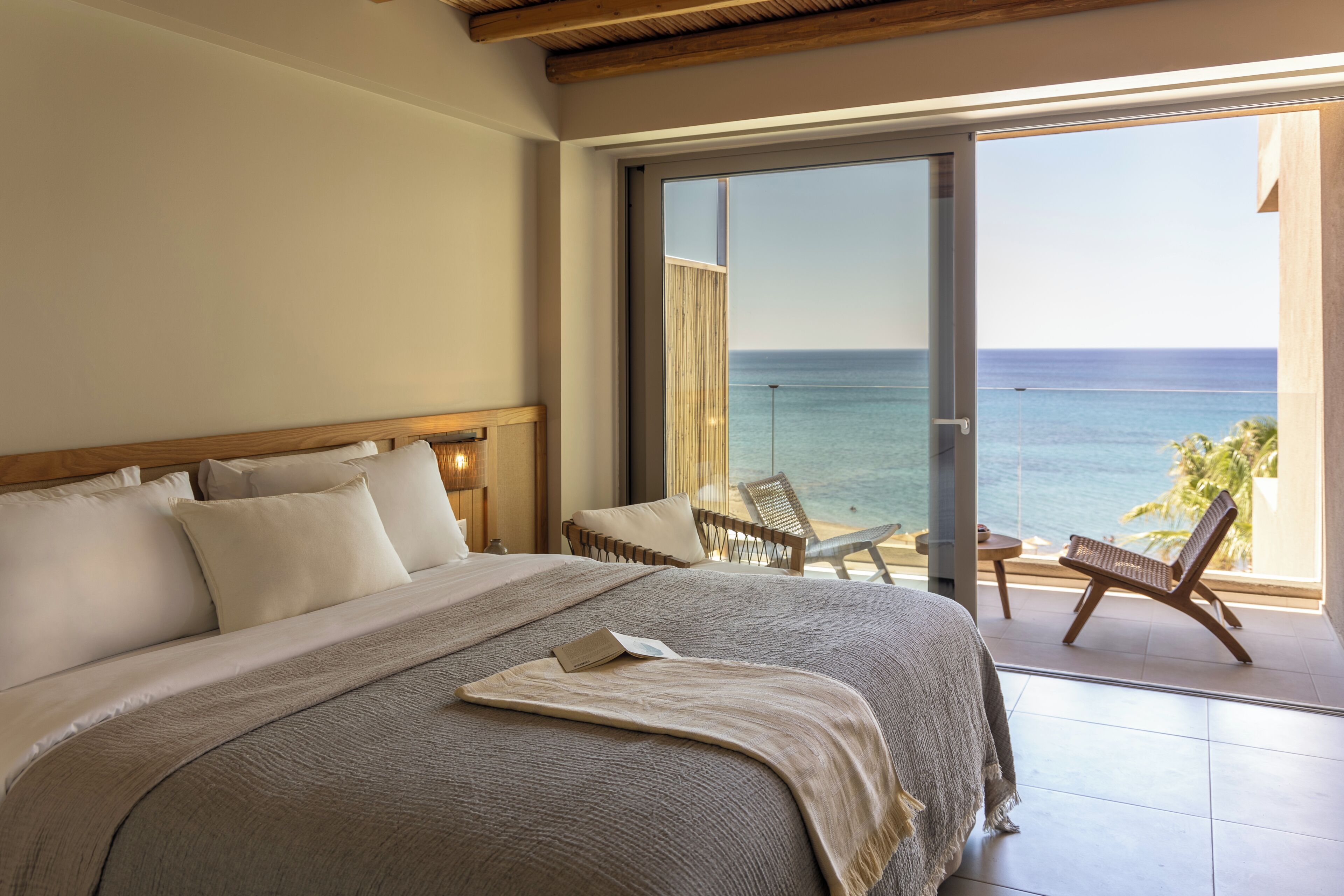Un dormitorio con una cama grande, vista al mar y un balcón con sillas.