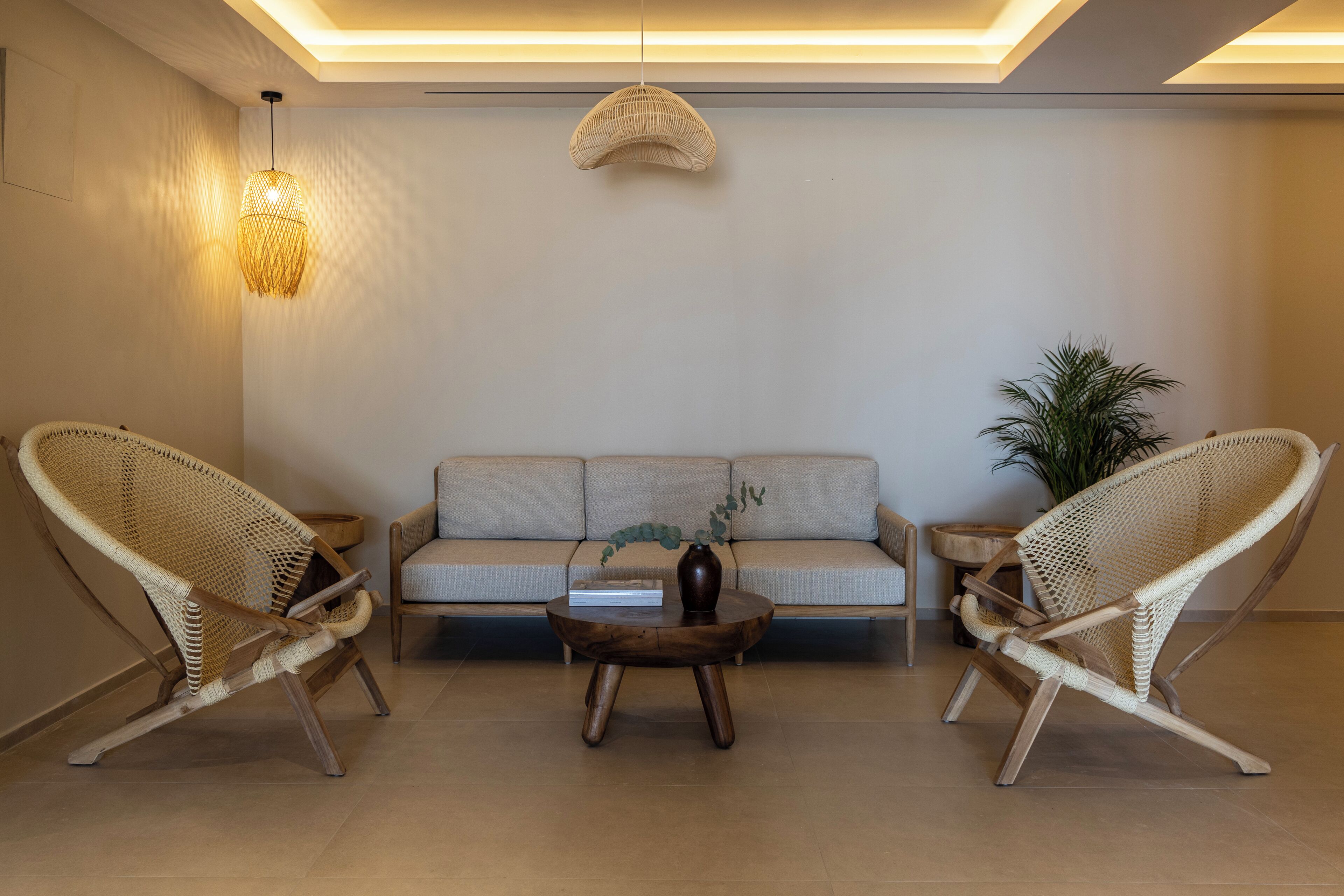 Una sala de estar moderna con un sofá, dos sillones de mimbre, una mesa baja y una lámpara colgante.