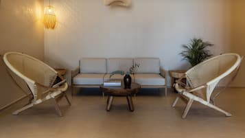 Una sala de estar moderna con un sofá, dos sillones de mimbre, una mesa baja y una lámpara colgante.