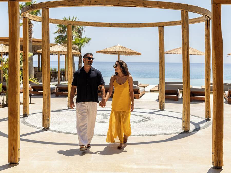 A wooden gazebo with a circular floor, palm trees, and lounge chairs in the background.