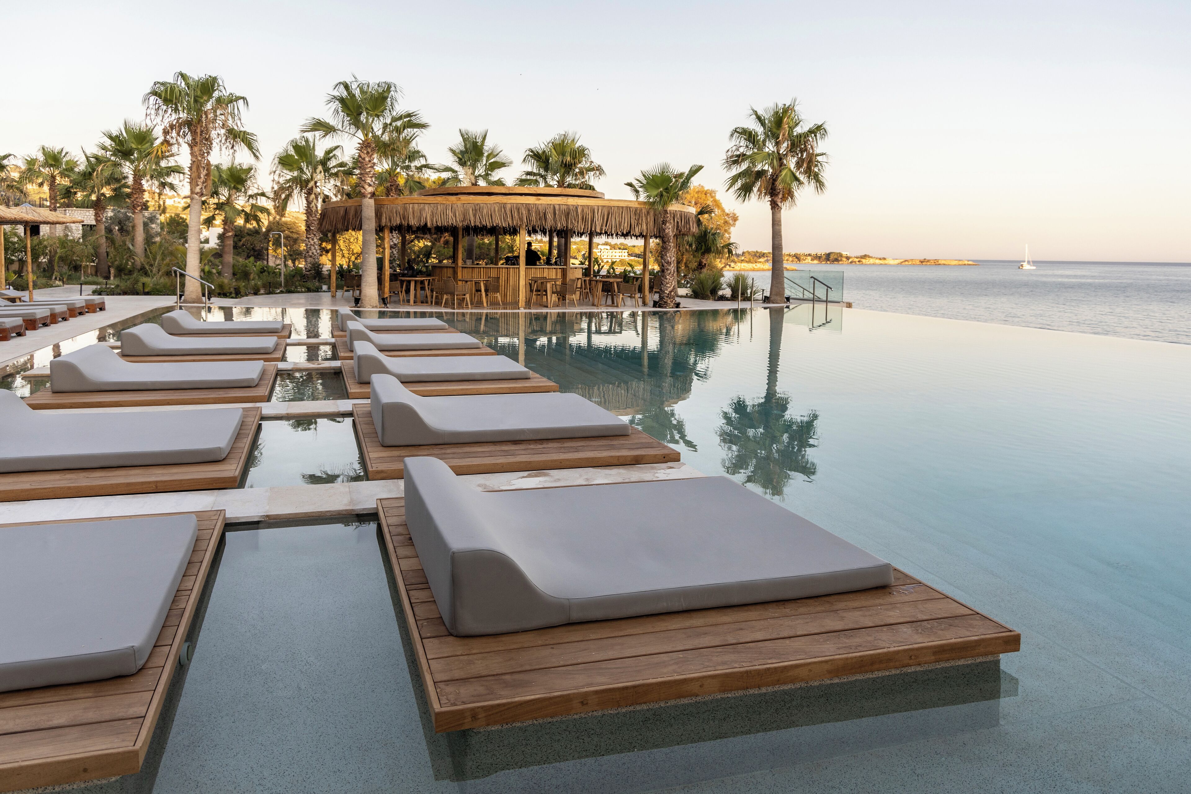 En infinitypool med solstolar och en bar med ett halmtak.