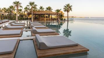 Una piscina infinita con sillones de descanso y un área de bar con techo de paja.