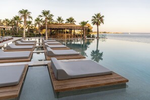 Una piscina infinita con sillones de descanso y un área de bar con techo de paja.