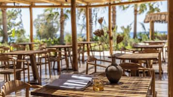 An outdoor dining area with wooden tables and chairs, a vase with dried flowers, and a glass of drink on a menu.