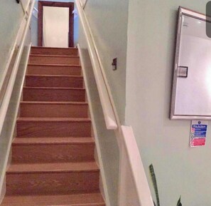 Eine Treppe mit Handlauf, eine Tür oben und ein Feueralarmschild an der Wand.