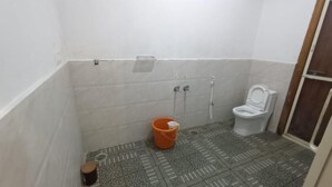 Et badeværelse med toilet, bruser og en balje.