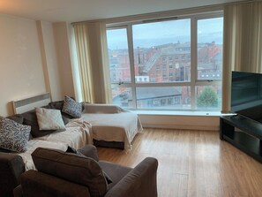Ein modernes Wohnzimmer mit großem Fenster, Flachbildfernseher und einer Sofagarnitur.