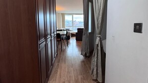 Un pasillo con suelo de madera, un comedor con sillas y mesa, y una vista a través de una ventana.
