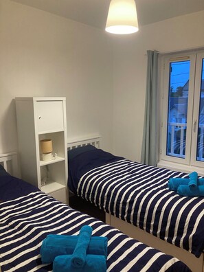 Ein Zimmer mit zwei Betten, einem Schrank, einer Lampe und einem Fenster mit Vorhängen.