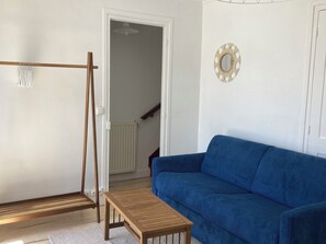 Ein Zimmer mit einem blauen Sofa, einem Holztisch, einer Holzschaukel und einer weißen Tür.