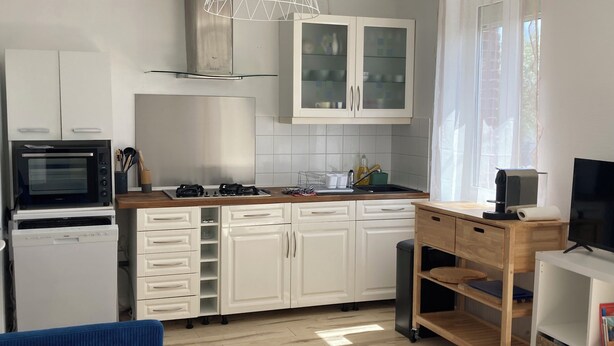 A modern kitchen with white cabinets, a built-in oven, a gas stove, and a wooden dining table. - Cosy house - walking distance to beach and market (Dives-sur-Mer)