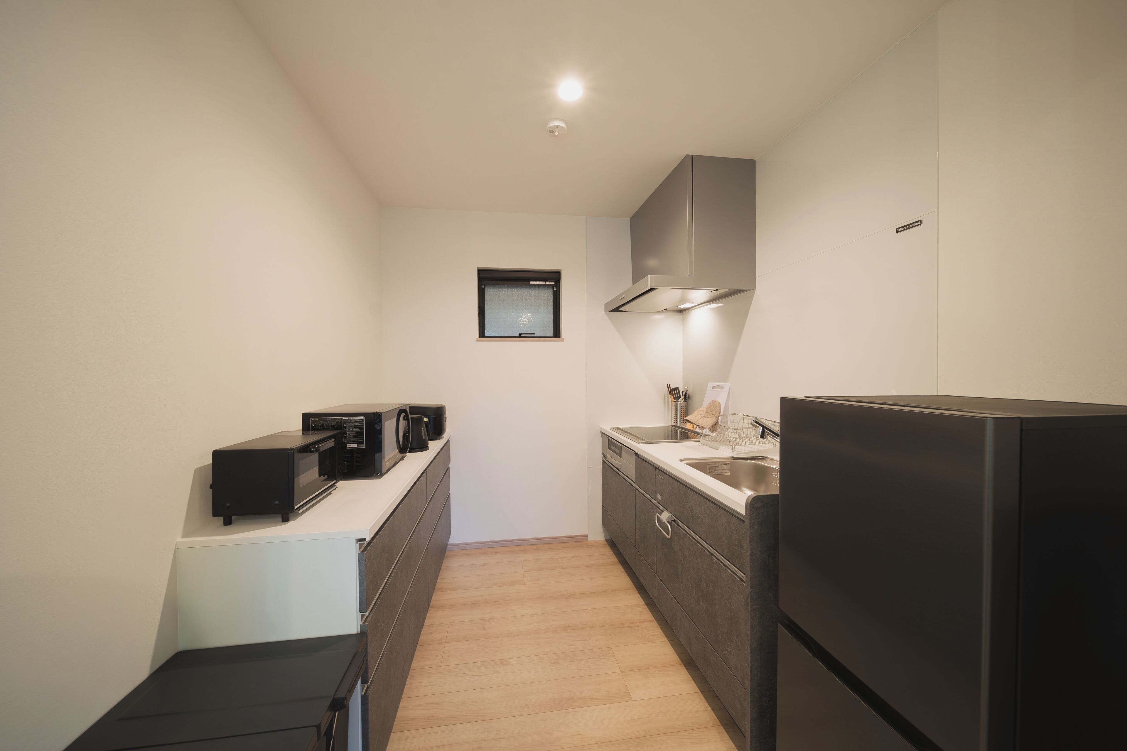 Eine kleine Küche mit Mikrowelle, Toaster und Kühlschrank, einem kleinen Fenster und einer Deckenleuchte.