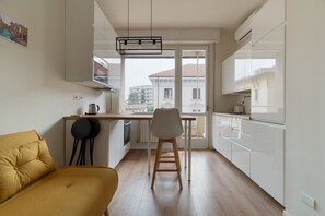 Eine kompakte Küche mit Essbereich, einer Couch und Blick auf Gebäude durch das Fenster.