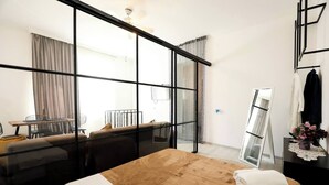 Une chambre d’hôtel avec un grand lit, un bureau avec une chaise, un miroir et une vue à travers une paroi en verre.