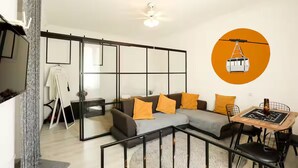 A modern living room with a sectional sofa, a dining table with chairs, a ceiling fan, and a large window.