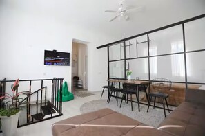 Ein modernes Wohnzimmer mit einer Couch, einem Esstisch mit Stühlen, einem an der Wand befestigten Fernseher und einem großen Fenster mit Blick.