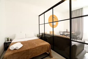 Une chambre d’hôtel comprenant un lit, une petite table avec une lampe, un canapé et un coin repas avec des chaises.