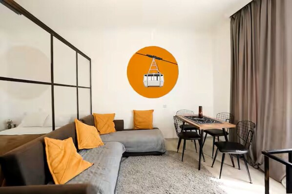 Un salon moderne avec un canapé d’angle, une table à manger avec des chaises et une grande fenêtre avec des rideaux.