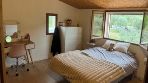 Um quarto com cama, escrivaninha, cadeira, cômoda e janela.