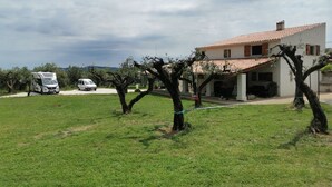 Uma casa com telhado de telhas, entrada para carros e veículos estacionados.
