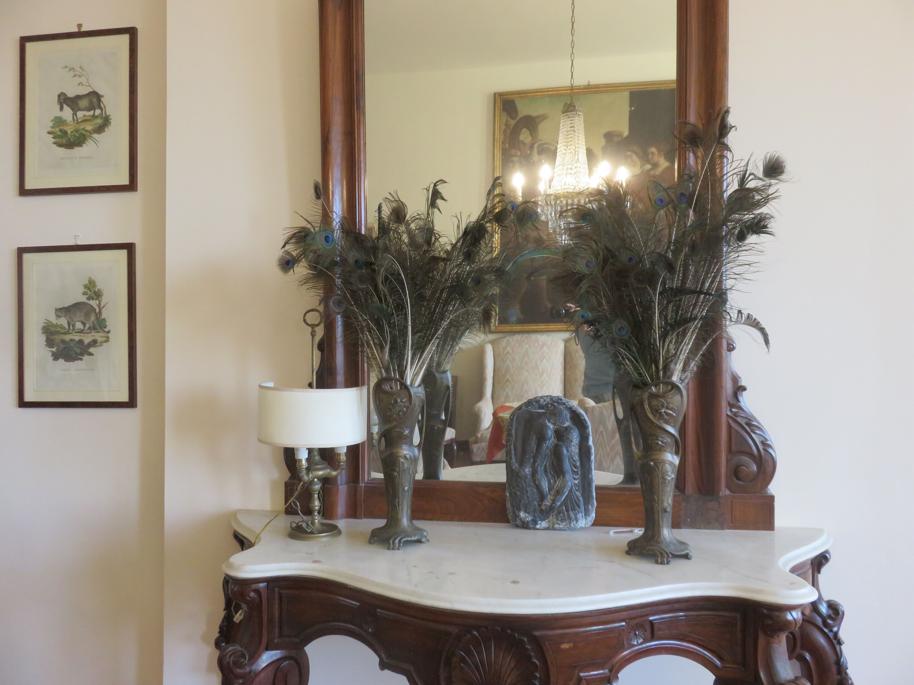 Una consola de madera con un espejo, jarrones decorativos e impresiones botánicas enmarcadas.