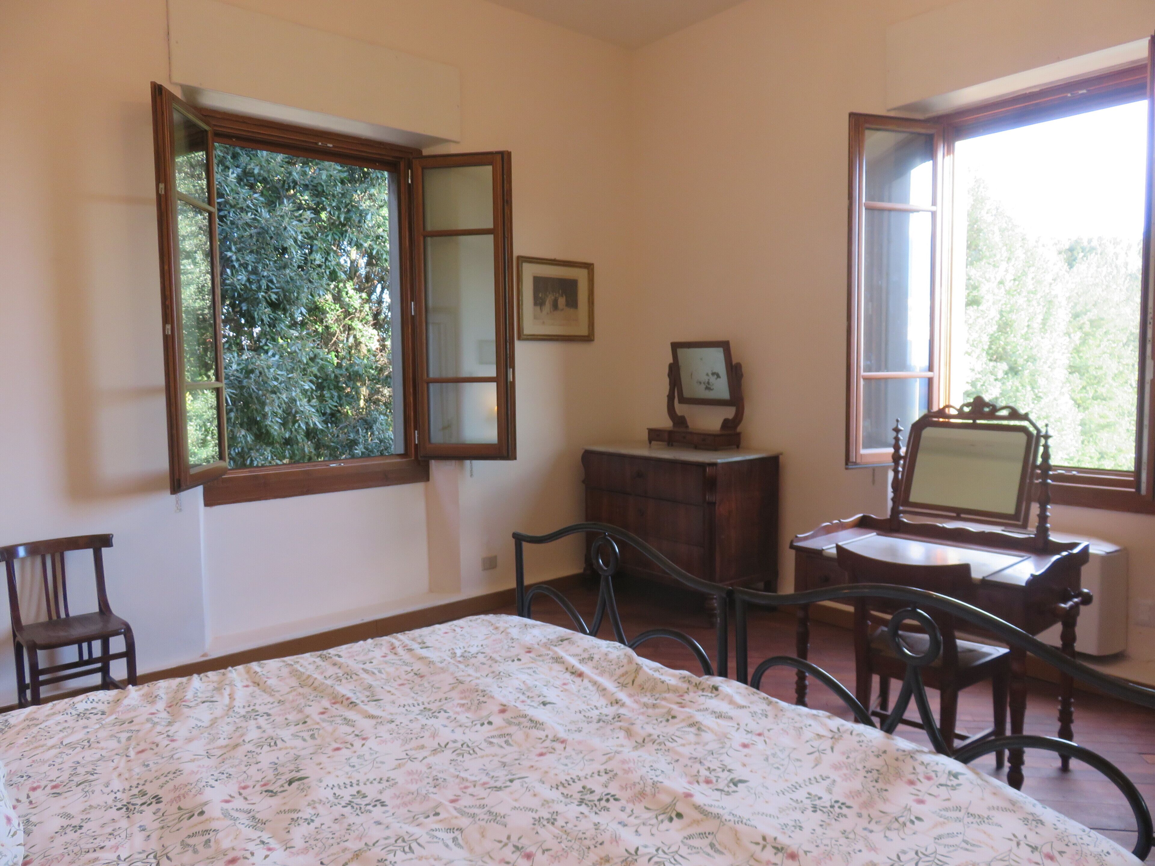 Une pièce comprenant un lit, un bureau avec une chaise, une commode et deux fenêtres dont les volets sont ouverts.