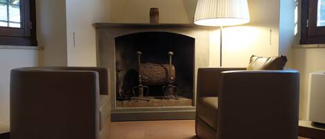 A living room with a fireplace, two armchairs, and a lamp.
