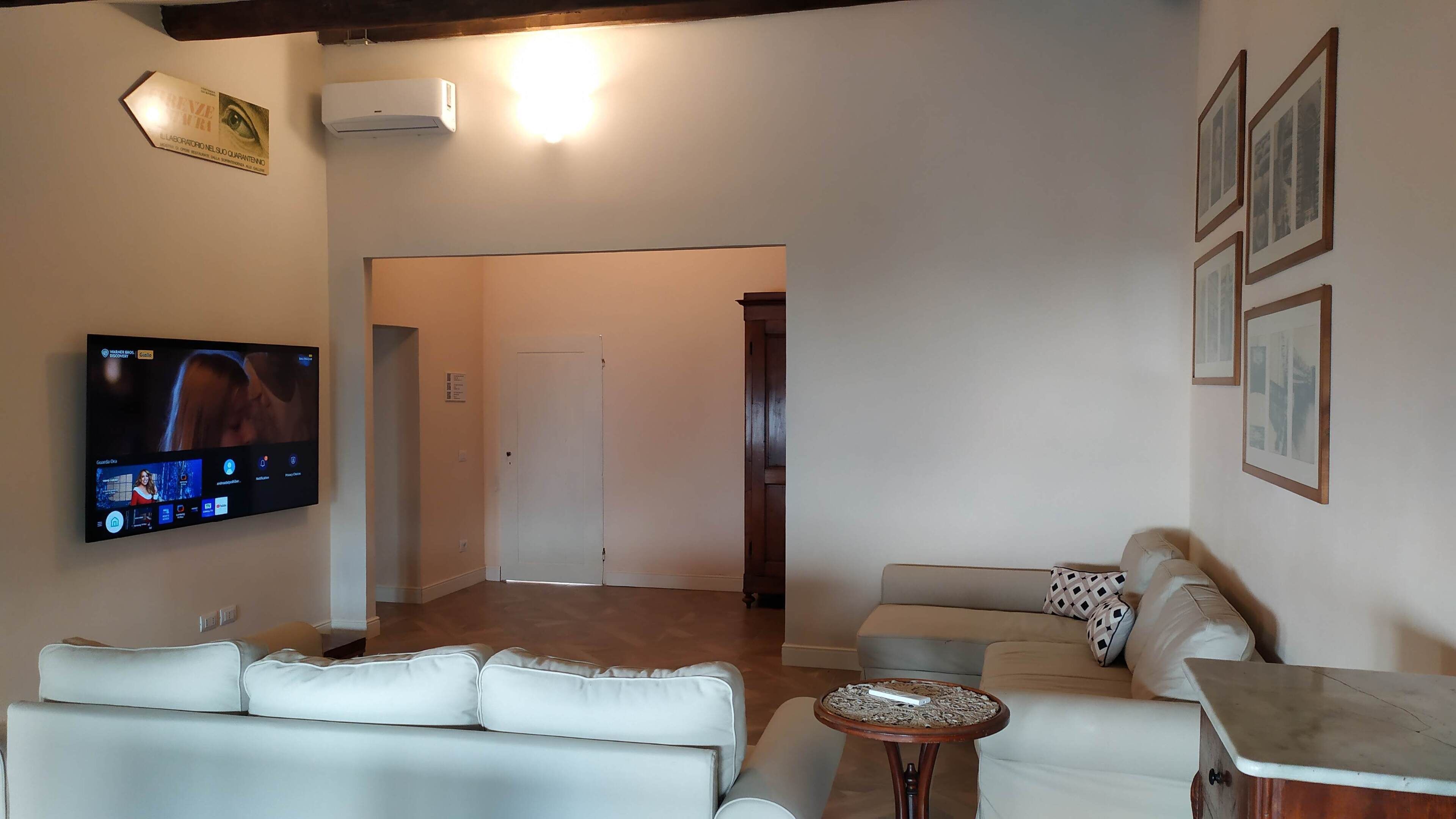Ein Wohnzimmer mit Flachbildfernseher, einem weißen Sofa, einem Holztisch und einem gerahmten Bild an der Wand.