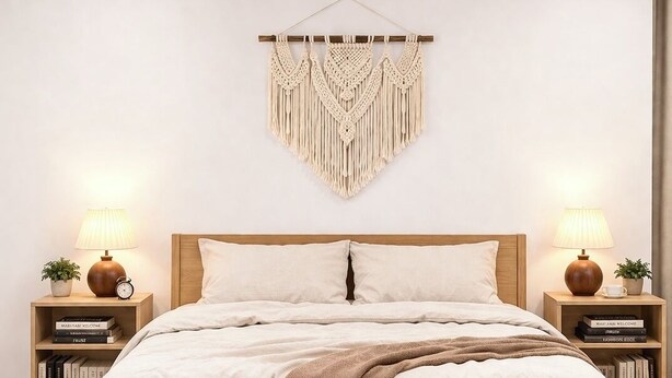 Quarto com cama, duas mesas de cabeceira, um pendente de macramé e um criado-mudo com abajur e livros.