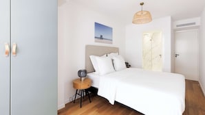 A bedroom with a bed, a nightstand, a lamp, a picture on the wall, and a door. - Quartier Carlton 3 rooms South with terrace (Cannes)